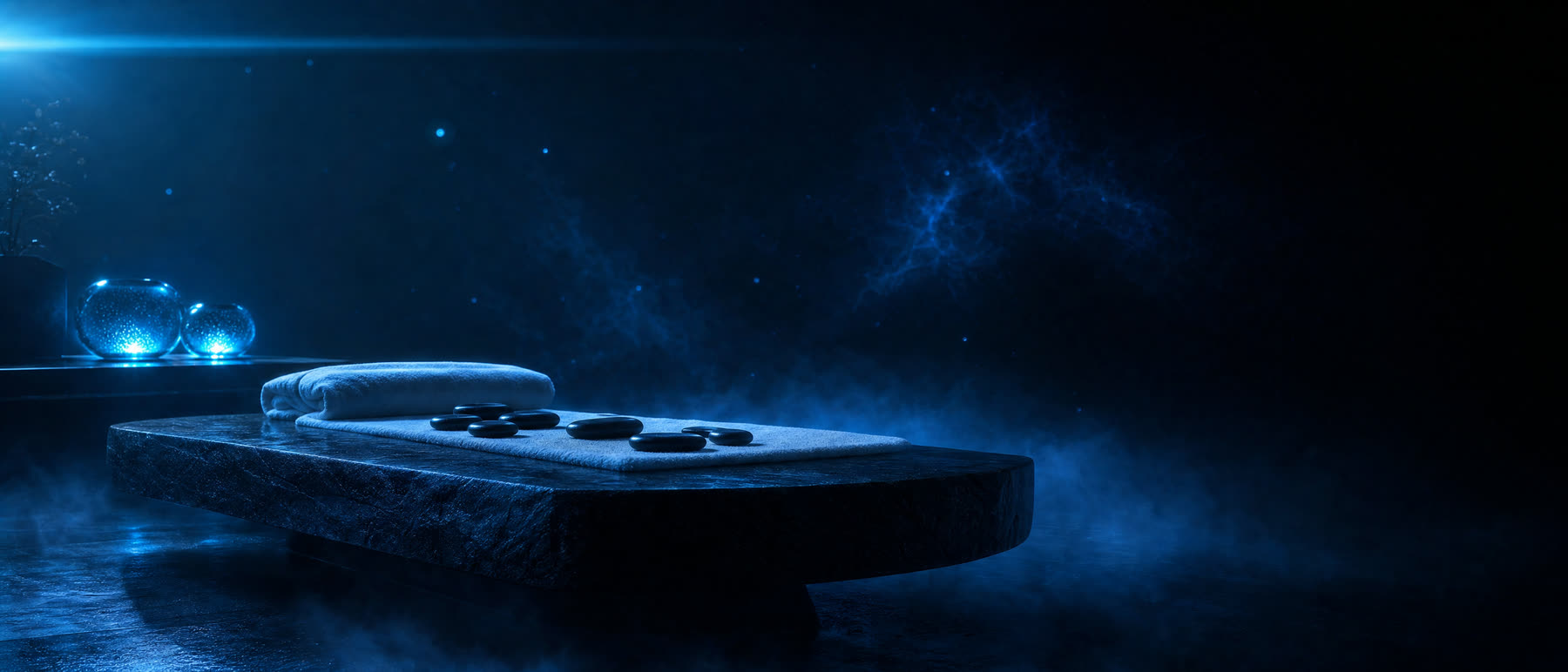 Serene minimalist spa room with a dark stone massage table, folded linen, smooth river stones, and glowing cyan candles